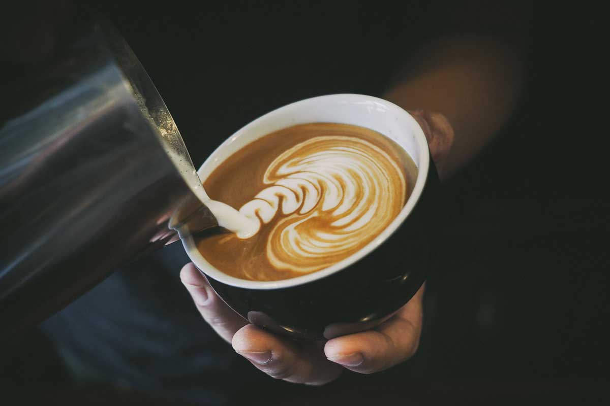 barista pouring the perfect cup of coffee using the creamer to make art